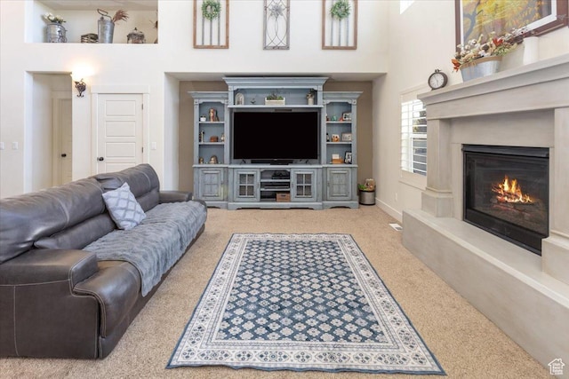 carpeted living room featuring a towering ceiling and a glass covered fireplace