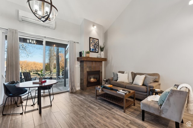 living area featuring an inviting chandelier, a wall mounted air conditioner, a tiled fireplace, wood finished floors, and high vaulted ceiling