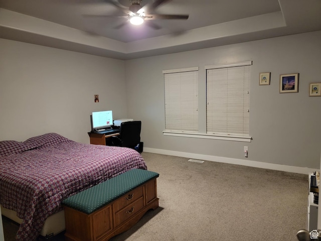 carpeted bedroom featuring visible vents, baseboards, a raised ceiling, and ceiling fan