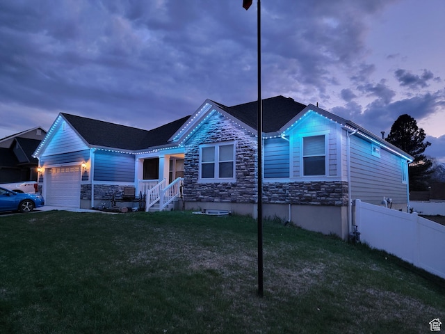 view of front of house with a lawn, stone siding, fence, and an attached garage