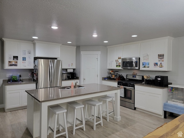 kitchen featuring stainless steel appliances, light wood-type flooring, a sink, and white cabinetry
