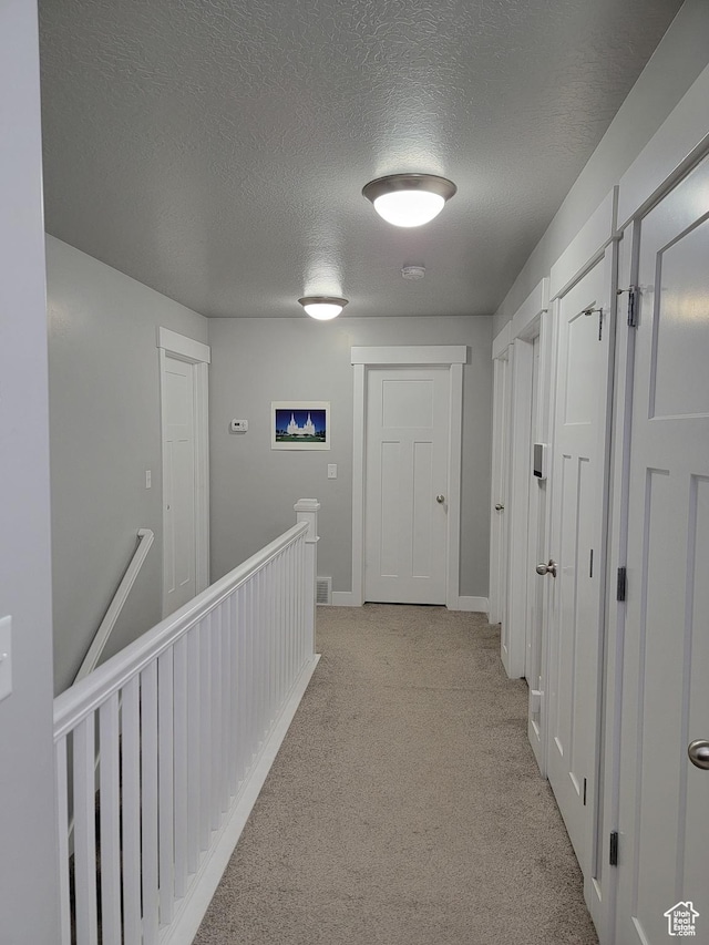 hall with light carpet, baseboards, an upstairs landing, and a textured ceiling