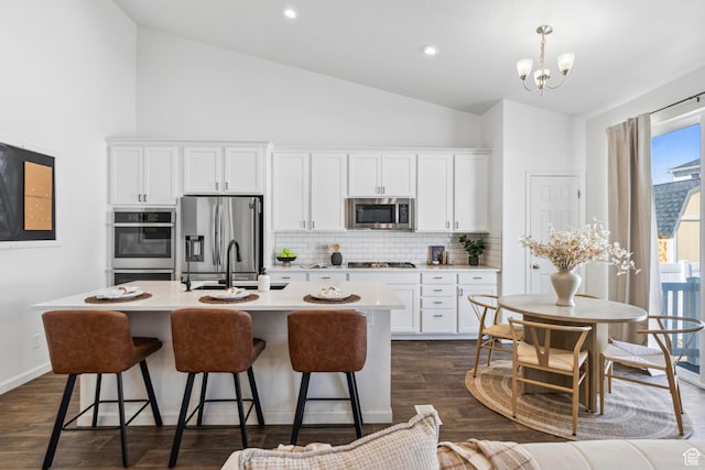 kitchen with appliances with stainless steel finishes, a kitchen island with sink, a breakfast bar area, decorative backsplash, and a sink