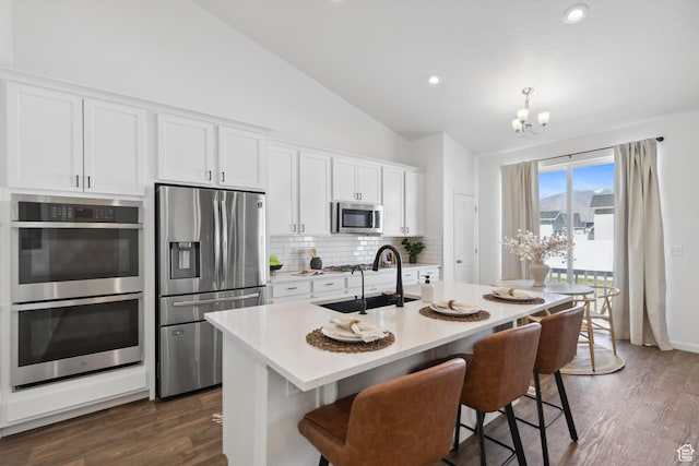 kitchen featuring vaulted ceiling, appliances with stainless steel finishes, a sink, a notable chandelier, and backsplash