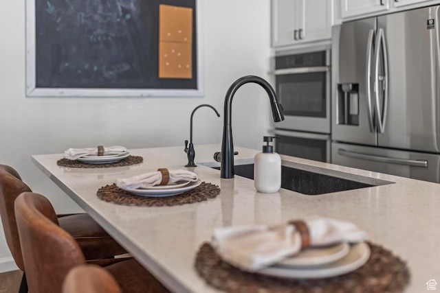 kitchen with stainless steel fridge, white cabinets, light stone countertops, a breakfast bar area, and a sink