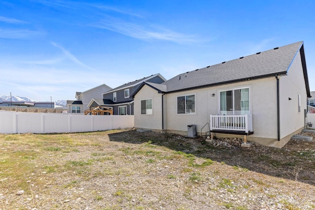 back of property with fence and a shingled roof