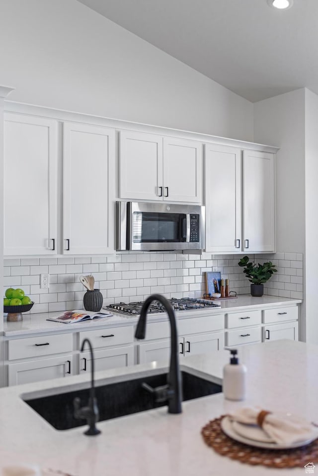 kitchen with vaulted ceiling, light countertops, backsplash, white cabinets, and stainless steel appliances