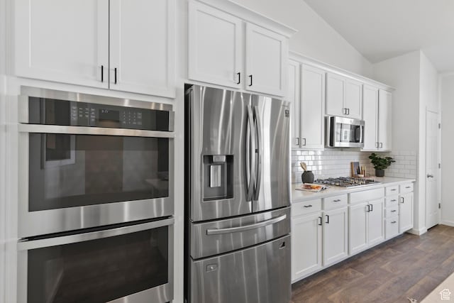 kitchen with appliances with stainless steel finishes, light countertops, white cabinetry, dark wood finished floors, and decorative backsplash