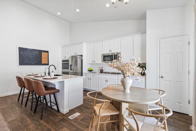 kitchen with high vaulted ceiling, a kitchen island with sink, visible vents, stainless steel appliances, and a sink