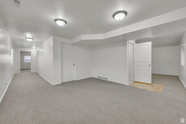 below grade area featuring a textured ceiling, baseboards, visible vents, and carpet floors