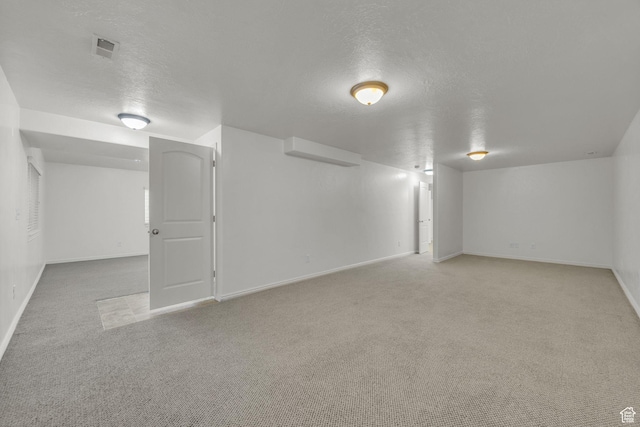 finished basement with light carpet, visible vents, baseboards, and a textured ceiling