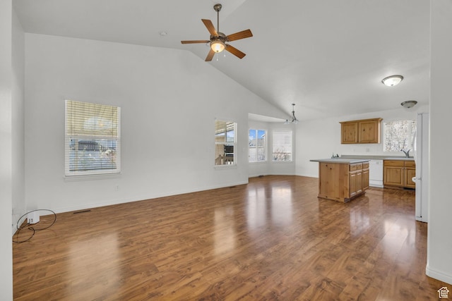 unfurnished living room with high vaulted ceiling, dark wood-style flooring, ceiling fan with notable chandelier, and baseboards
