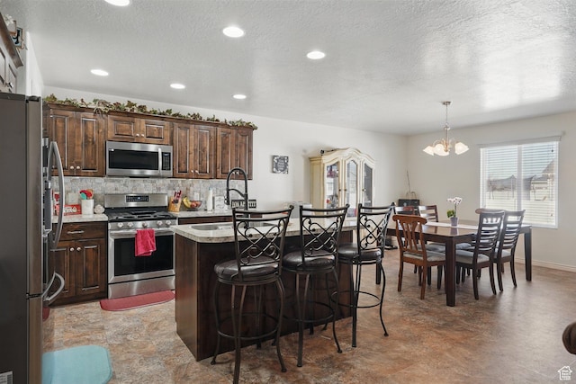 kitchen featuring tasteful backsplash, an island with sink, a chandelier, stainless steel appliances, and a breakfast bar area