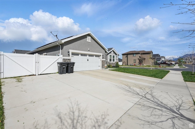 view of home's exterior featuring stucco siding, a gate, an attached garage, driveway, and a residential view