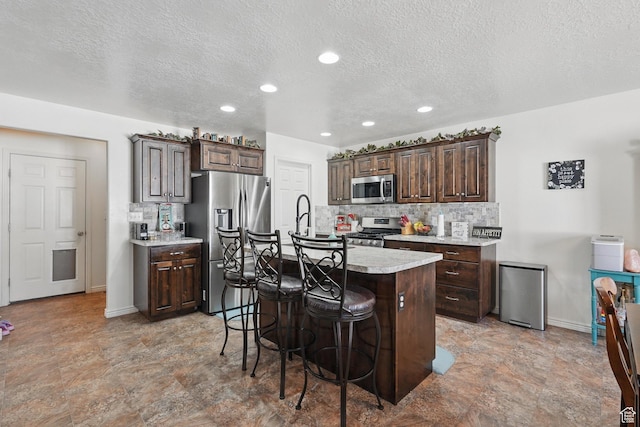 kitchen with a kitchen bar, appliances with stainless steel finishes, an island with sink, and dark brown cabinetry