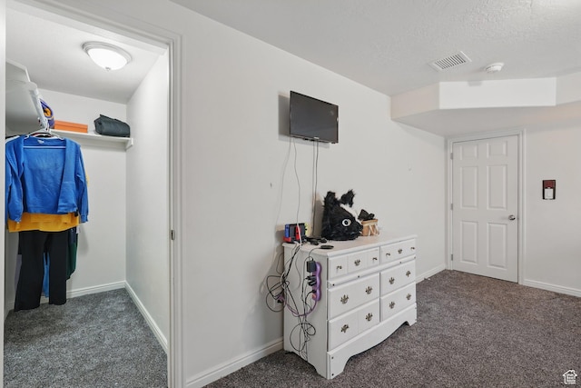 hallway with dark carpet, baseboards, visible vents, and a textured ceiling