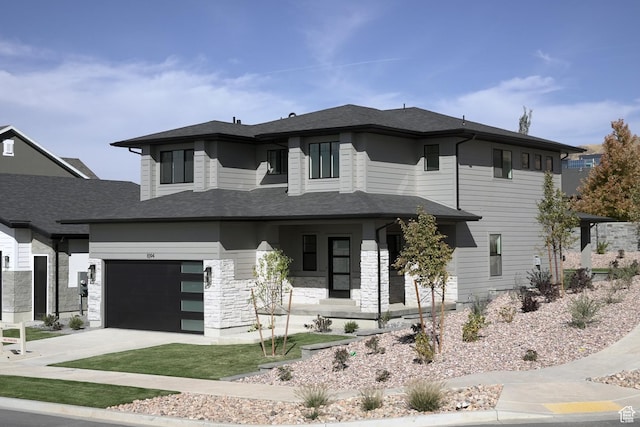 prairie-style house with a garage, covered porch, driveway, and stone siding