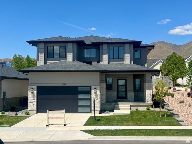 prairie-style home featuring an attached garage, stone siding, a front yard, a mountain view, and concrete driveway