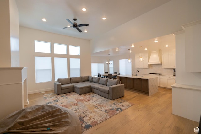 living area with recessed lighting, a ceiling fan, a towering ceiling, and light wood-style floors