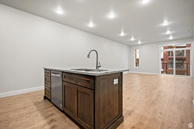 kitchen featuring dark brown cabinetry, light wood-type flooring, a sink, a center island with sink, and baseboards