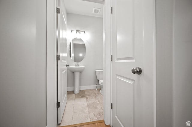 half bath featuring toilet, a sink, baseboards, and visible vents