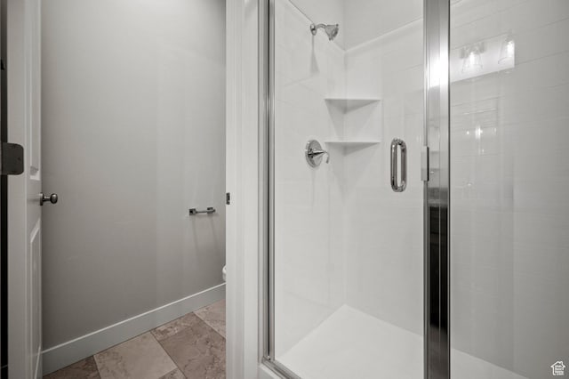 bathroom with toilet, baseboards, a stall shower, and stone finish flooring