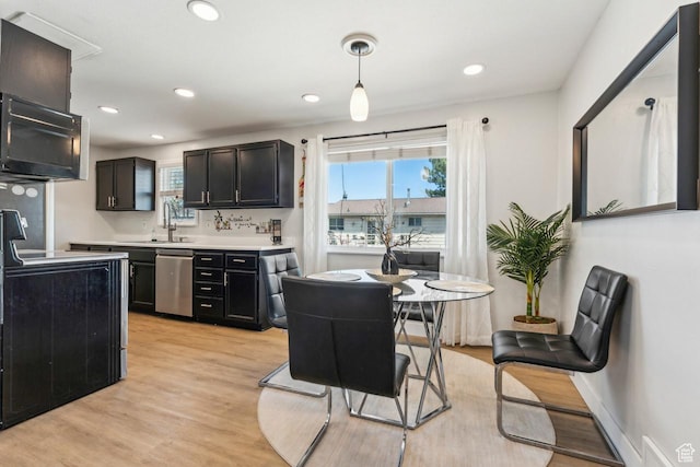 kitchen with dark cabinetry, light wood-type flooring, stainless steel dishwasher, and light countertops