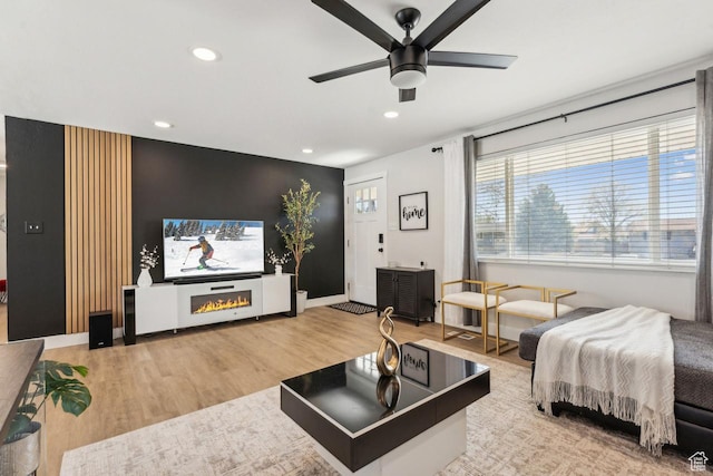 living area with wood finished floors, ceiling fan, an accent wall, and recessed lighting