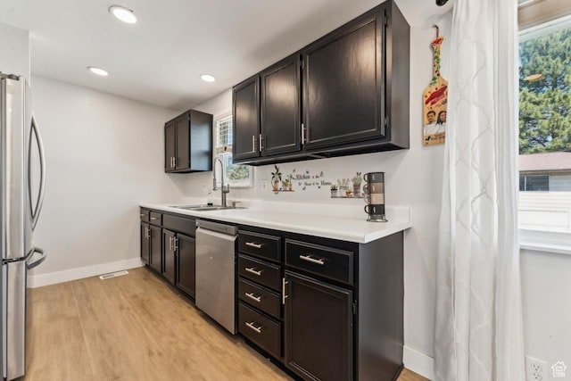 kitchen with baseboards, a sink, light countertops, stainless steel appliances, and light wood-style flooring