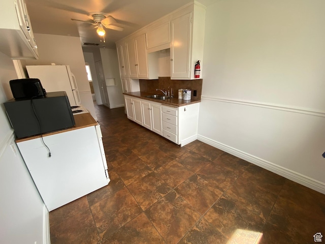 kitchen with a sink, dark countertops, baseboards, backsplash, and white cabinetry