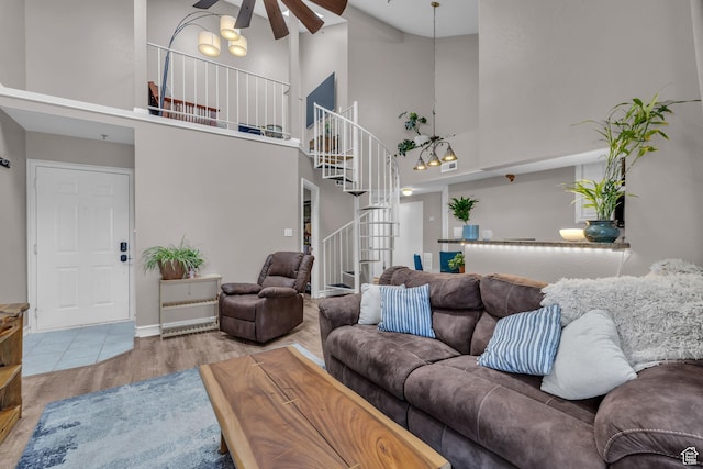 living area with ceiling fan, a high ceiling, wood finished floors, and stairs