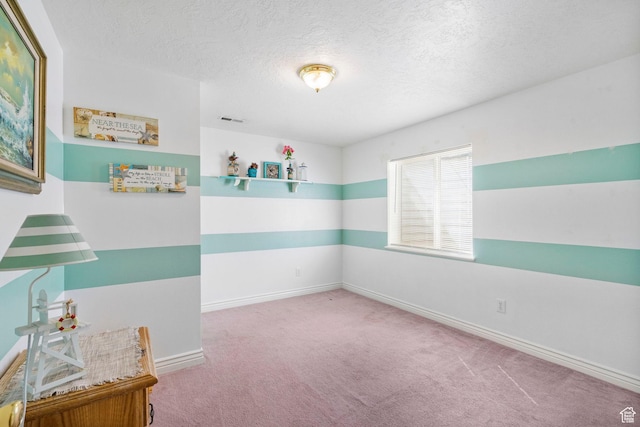 spare room featuring carpet floors, baseboards, visible vents, and a textured ceiling