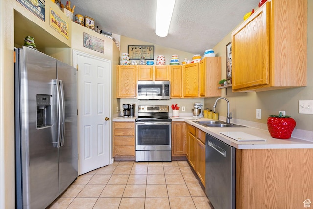 kitchen featuring appliances with stainless steel finishes, light tile patterned floors, a textured ceiling, lofted ceiling, and a sink