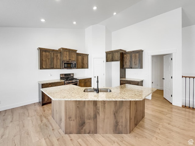 kitchen with a large island, light wood-style flooring, appliances with stainless steel finishes, high vaulted ceiling, and a sink