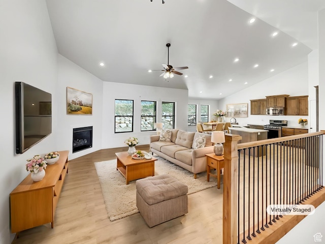 living area featuring a ceiling fan, light wood-style floors, recessed lighting, high vaulted ceiling, and a glass covered fireplace