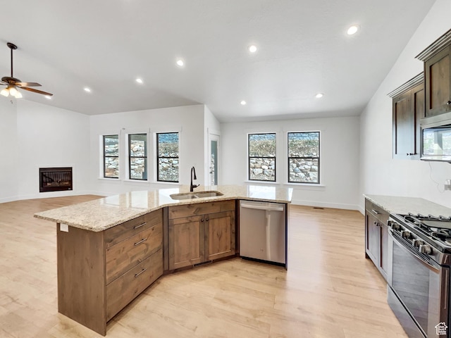 kitchen with a sink, light wood-style flooring, light stone counters, and stainless steel appliances