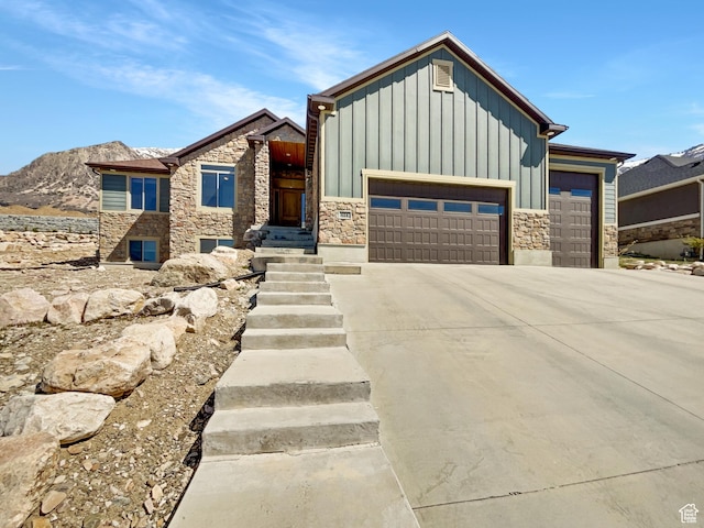view of front of home with board and batten siding, an attached garage, stone siding, and driveway