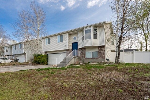 bi-level home featuring a garage, brick siding, driveway, and fence
