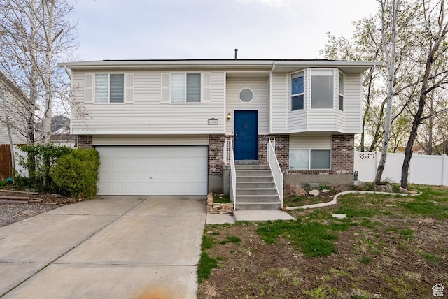raised ranch with concrete driveway, a garage, fence, and brick siding