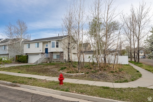 bi-level home with brick siding, driveway, fence, and a garage