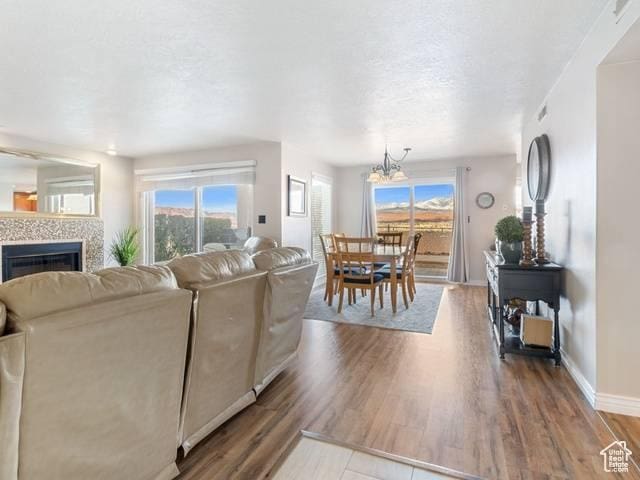 living area with a chandelier, a tiled fireplace, baseboards, and wood finished floors
