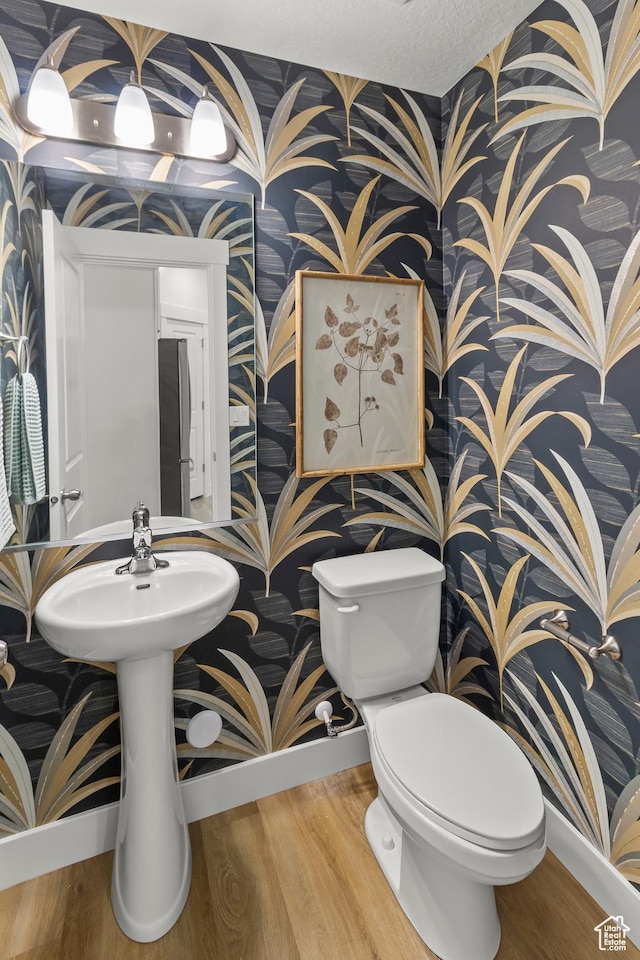 half bathroom featuring baseboards, wallpapered walls, and toilet