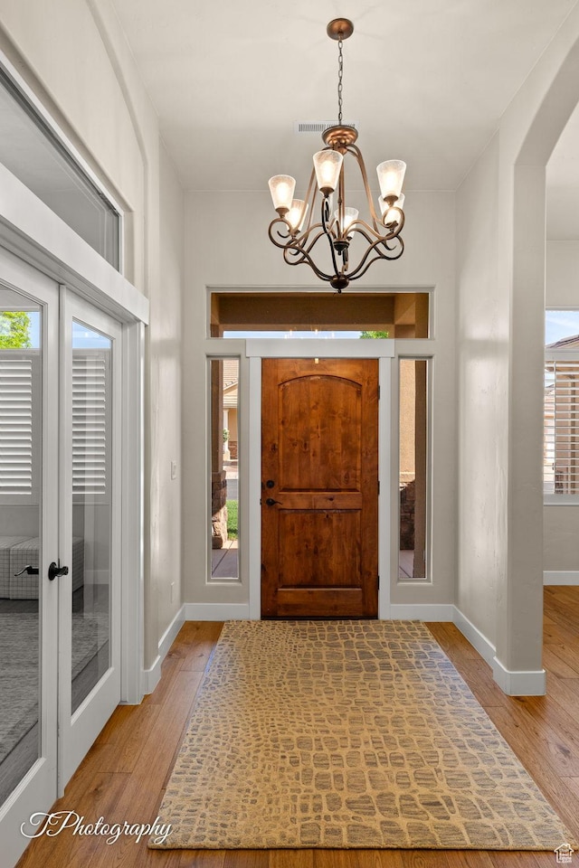 foyer featuring a chandelier, arched walkways, baseboards, and wood finished floors