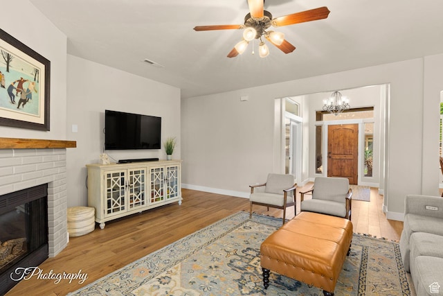 living room with a brick fireplace, ceiling fan with notable chandelier, baseboards, and wood finished floors