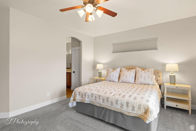 carpeted bedroom with arched walkways, ensuite bathroom, baseboards, and a ceiling fan