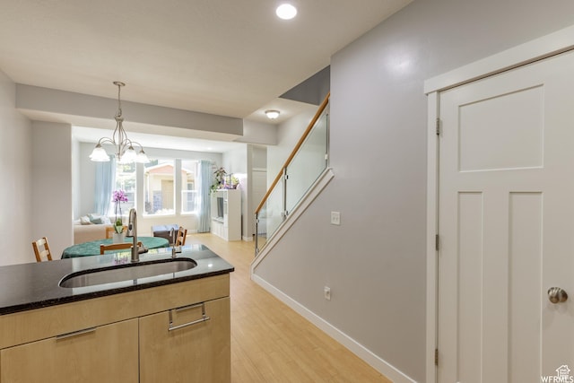 kitchen with dark stone countertops, hanging light fixtures, a sink, light brown cabinetry, and light wood finished floors