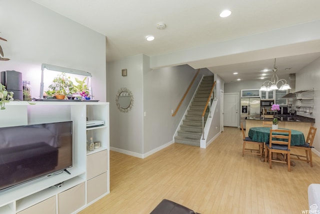 living room with light wood-style flooring, a chandelier, baseboards, and stairs
