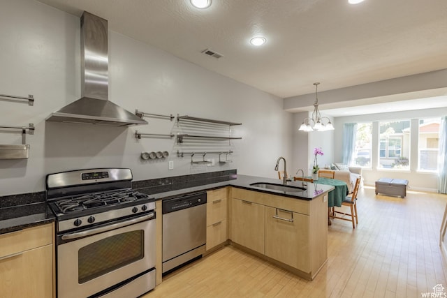 kitchen with light brown cabinets, a sink, wall chimney range hood, a peninsula, and stainless steel appliances