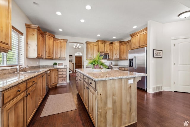 kitchen with light stone counters, a center island, visible vents, appliances with stainless steel finishes, and a sink