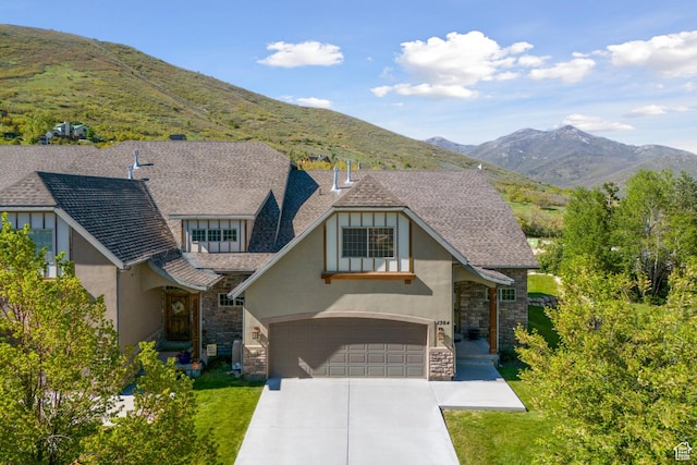 view of front of home with a garage, stucco siding, stone siding, a mountain view, and driveway
